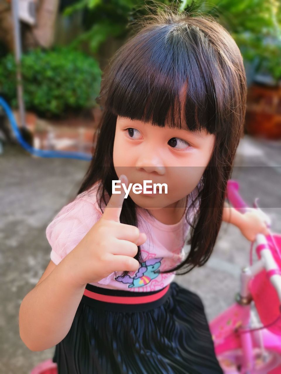 Cute girl with hand raised looking away while sitting outdoors