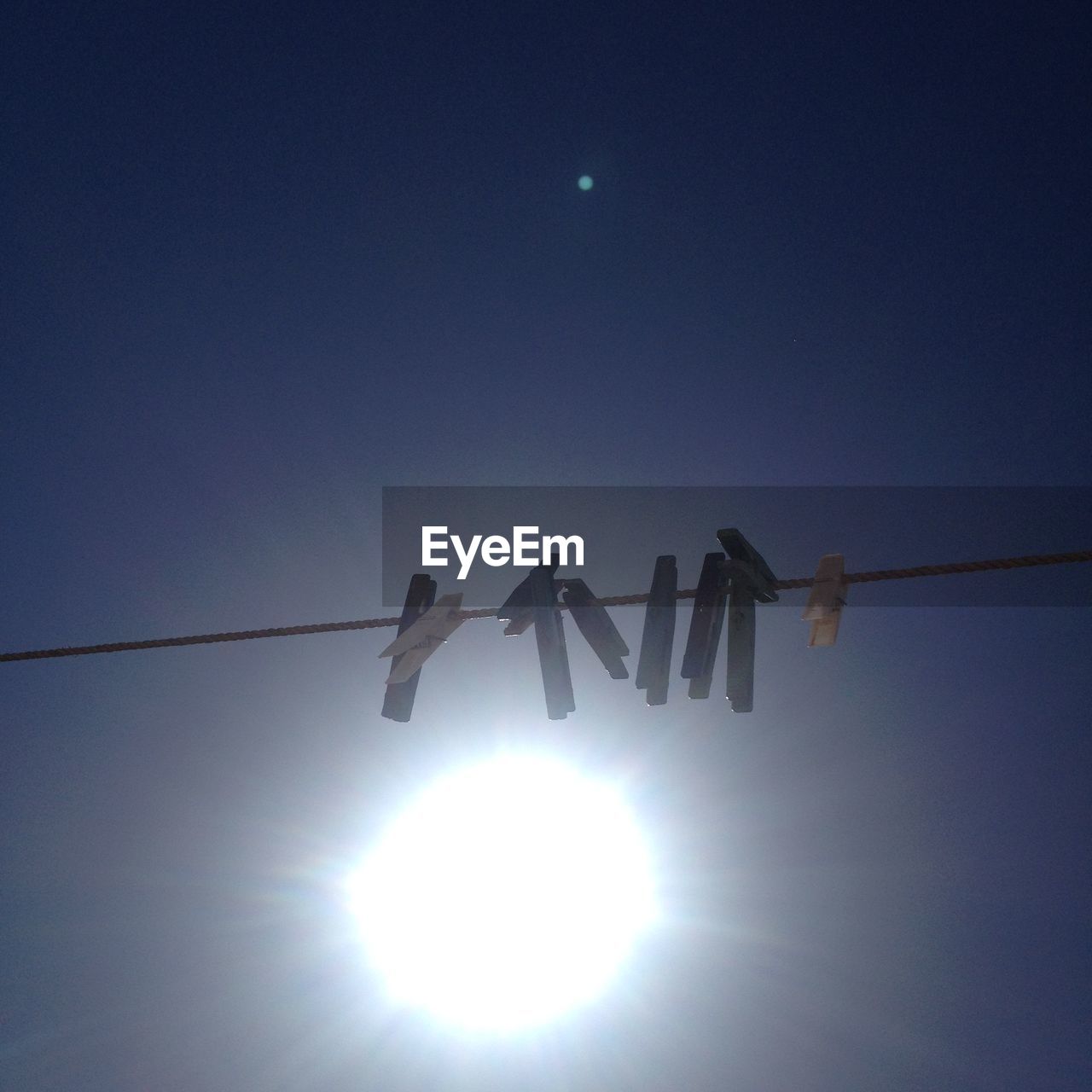 Low angle view of clothespins hanging on rope against sky on sunny day