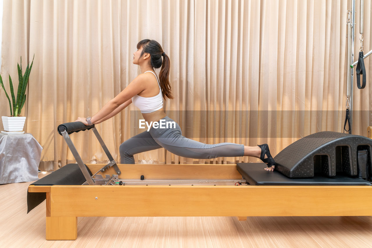 Young asian woman working on pilates reformer machine during exercise training to stretch her legs