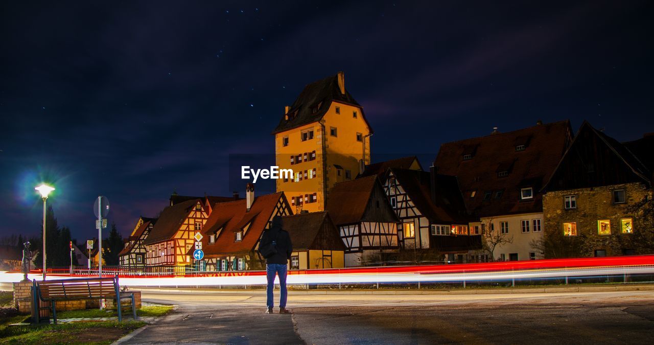 Light trails on road amidst buildings against sky at night