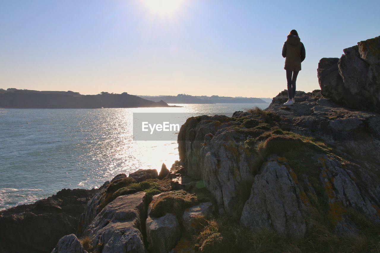 Rear view of girl on rocks by sea against sky