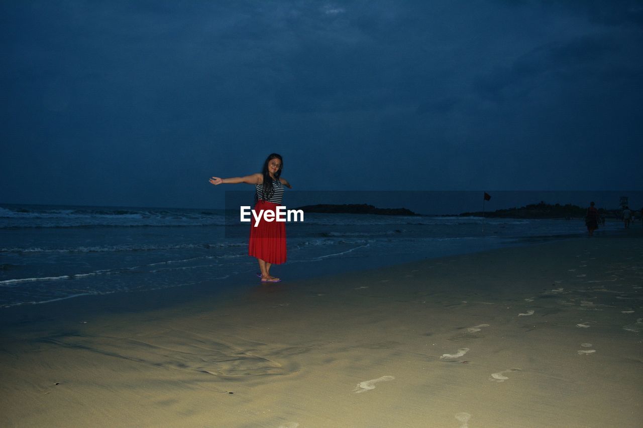 Woman with arms outstretched standing at beach against sky
 
