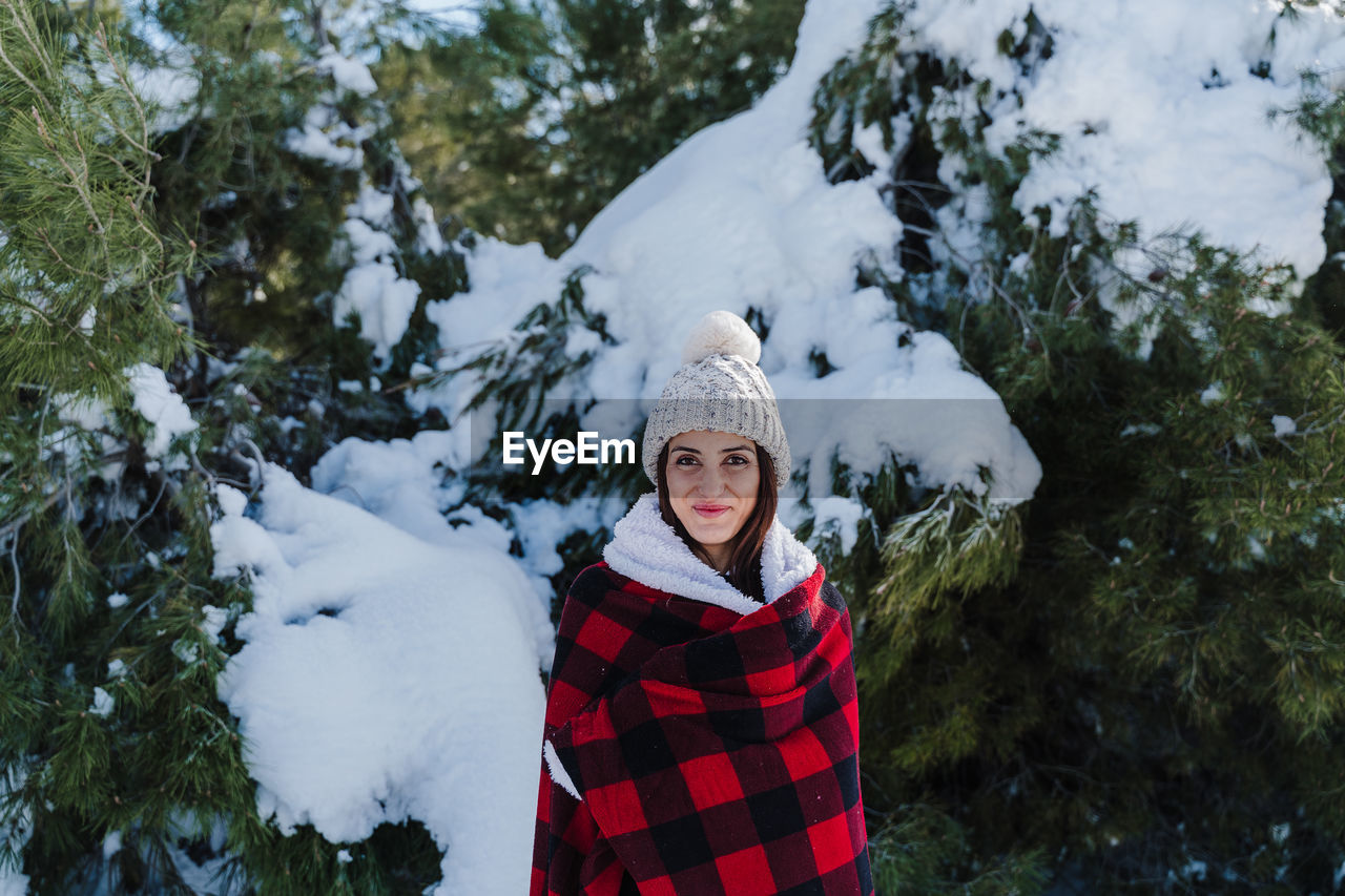 Portrait of woman standing against snow covered trees during winter