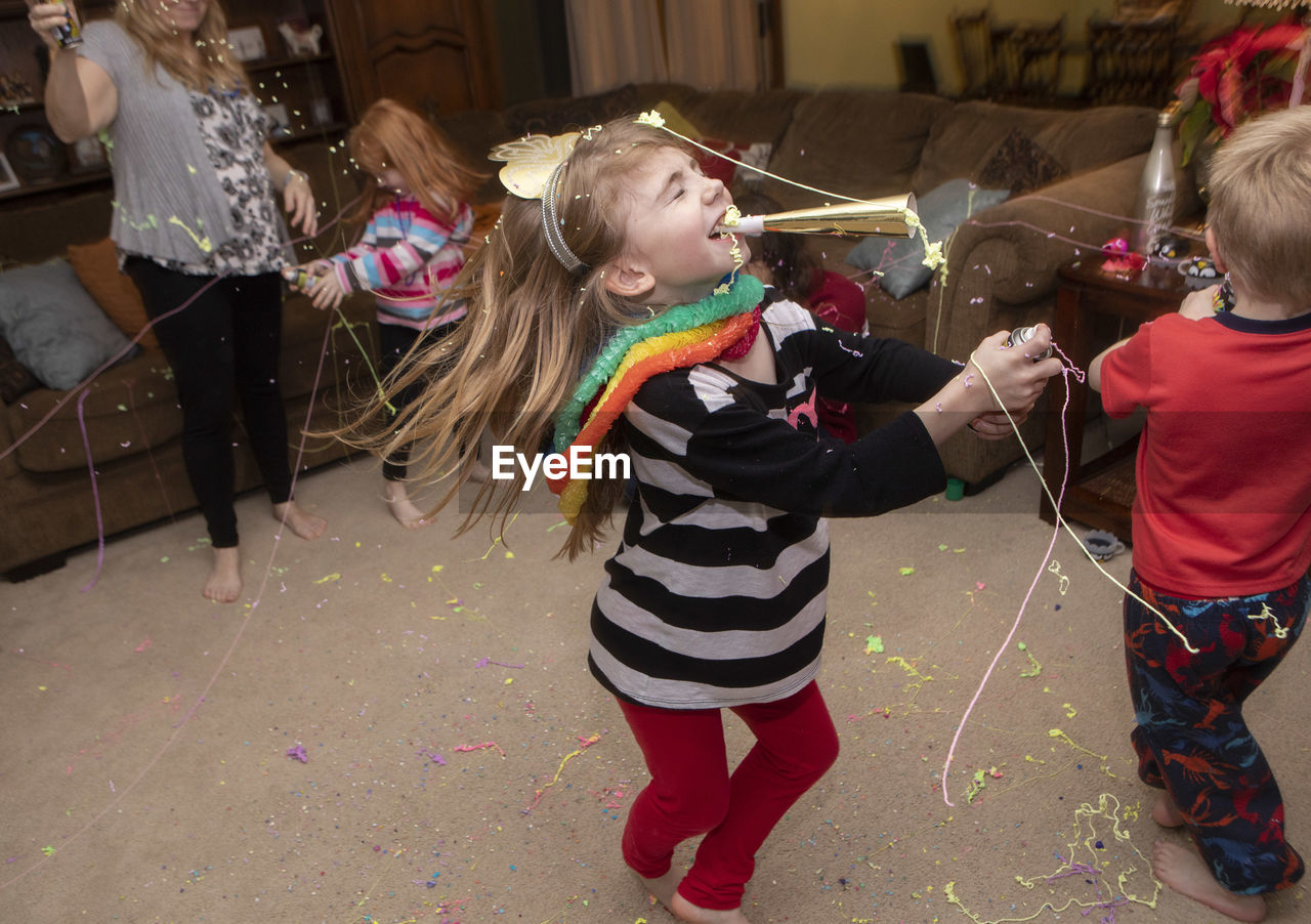 Girl blowing party horn blower during celebration in living room at home