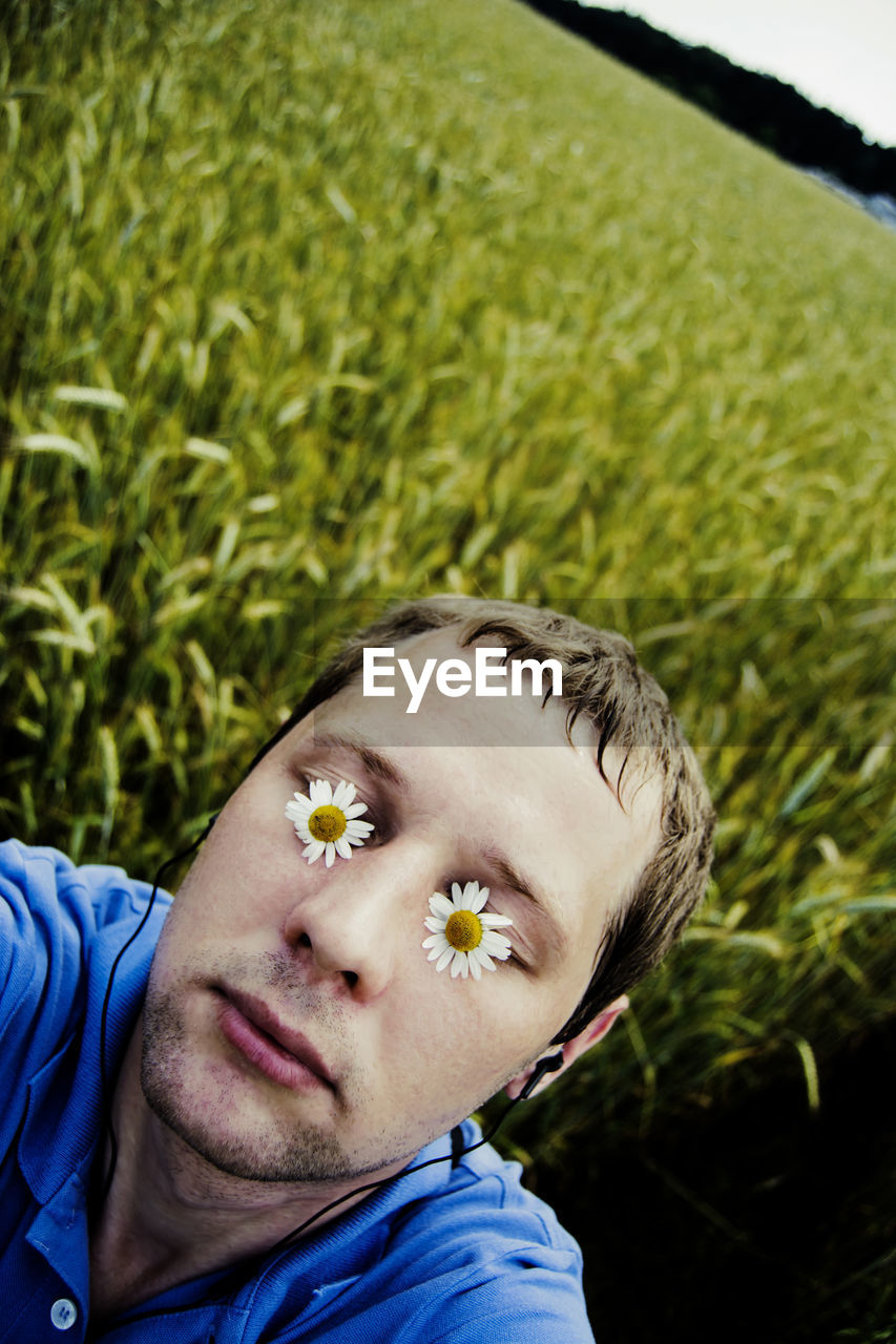 Close-up of man with eyes covered by flowers while listening to music on field