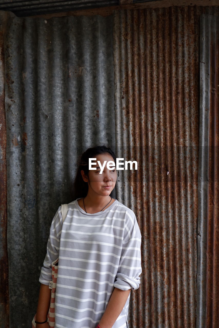 Young woman looking away while standing against wall