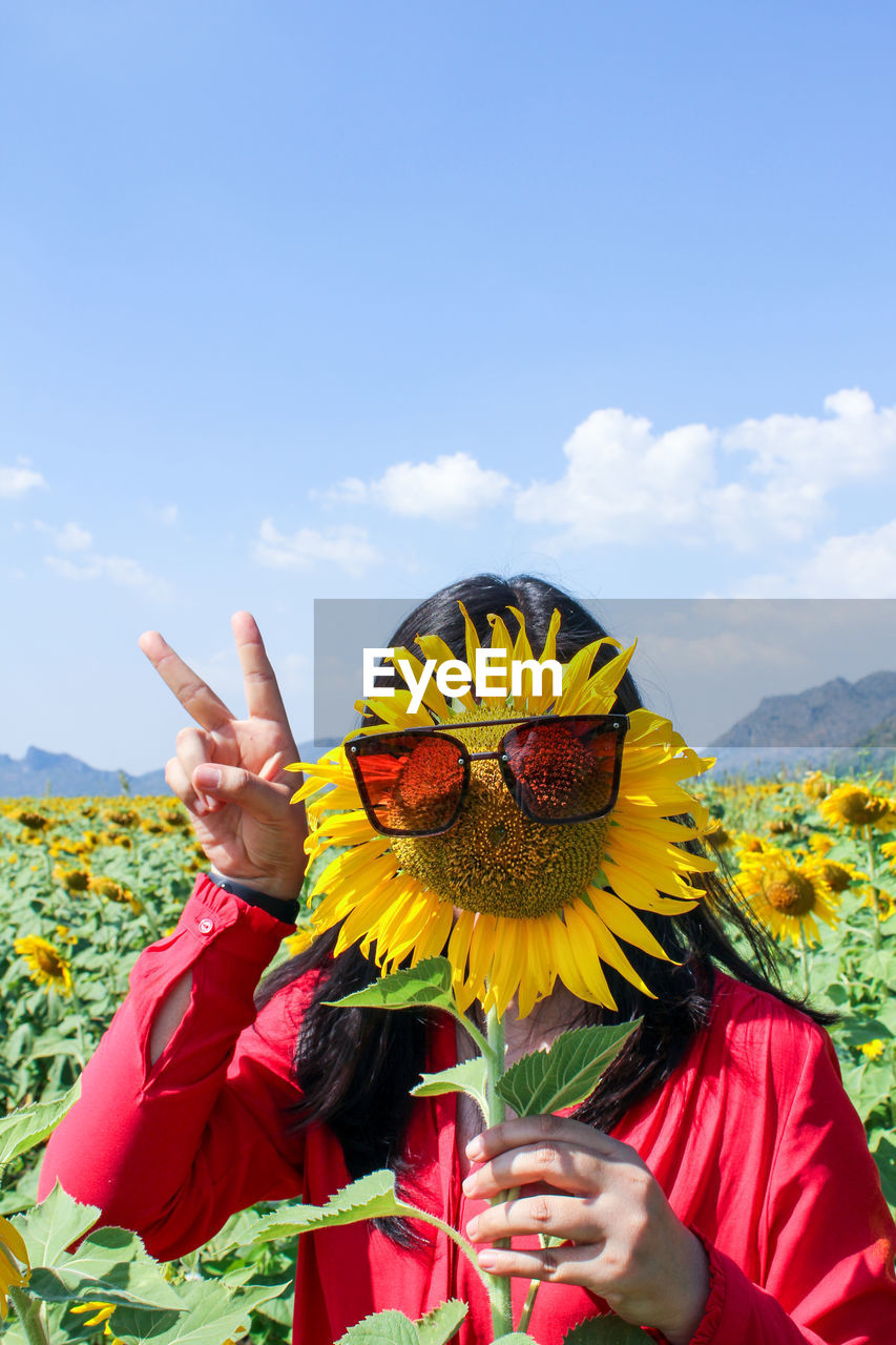 Woman holding sunflower with sunglasses against sky during sunny day