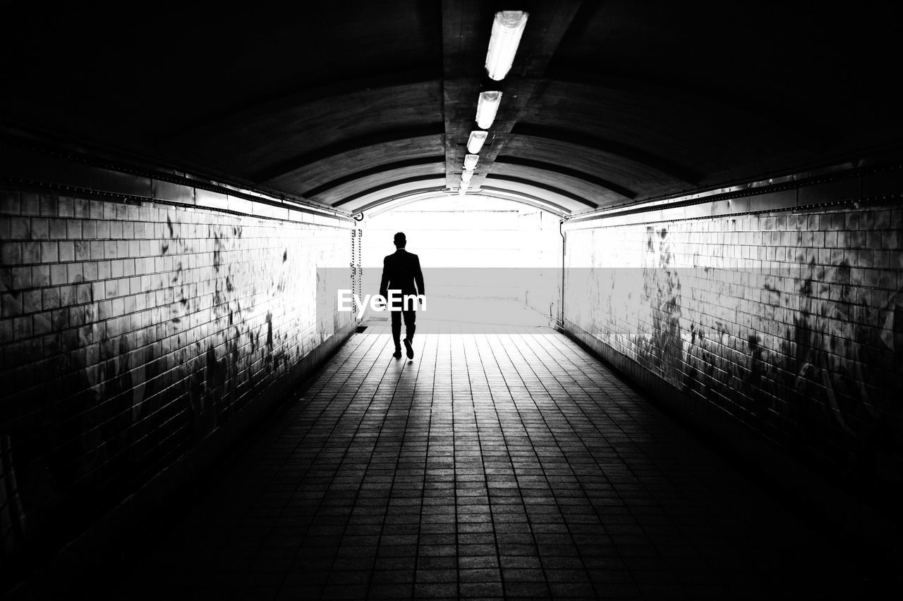 Silhouette man walking in illuminated tunnel