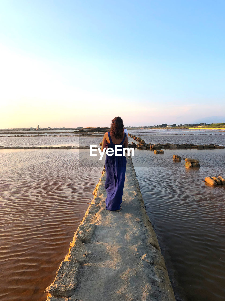 Rear view of woman standing on pier by water against sky