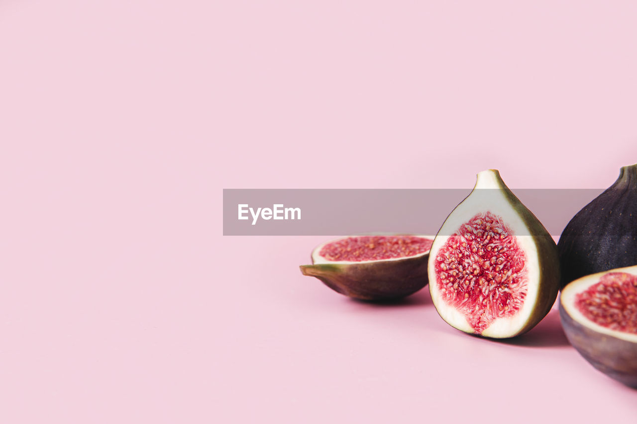 Fresh tasty fig fruit halves with shadow on pink background table with empty copy space