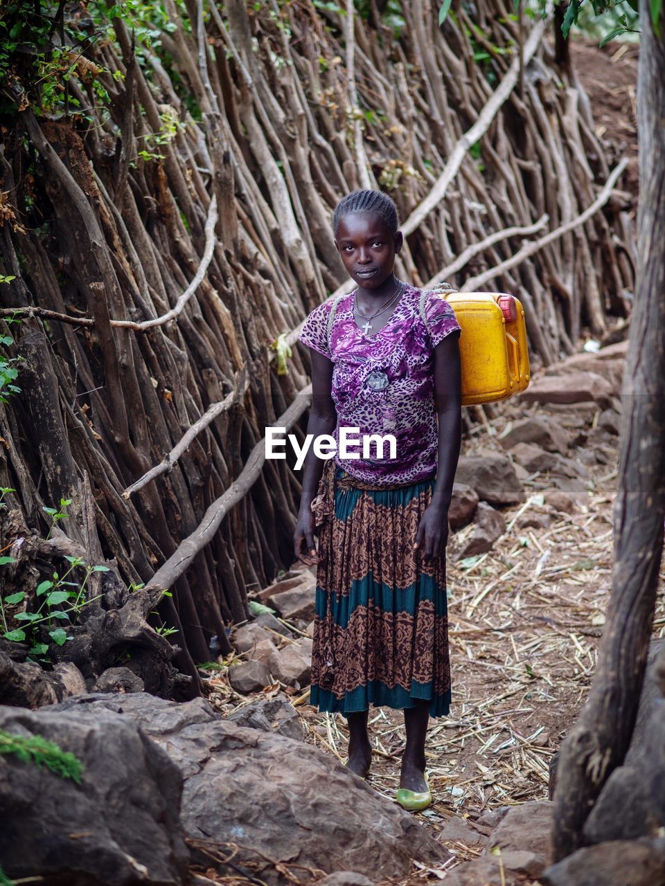 PORTRAIT OF A SMILING WOMAN STANDING AGAINST TREES