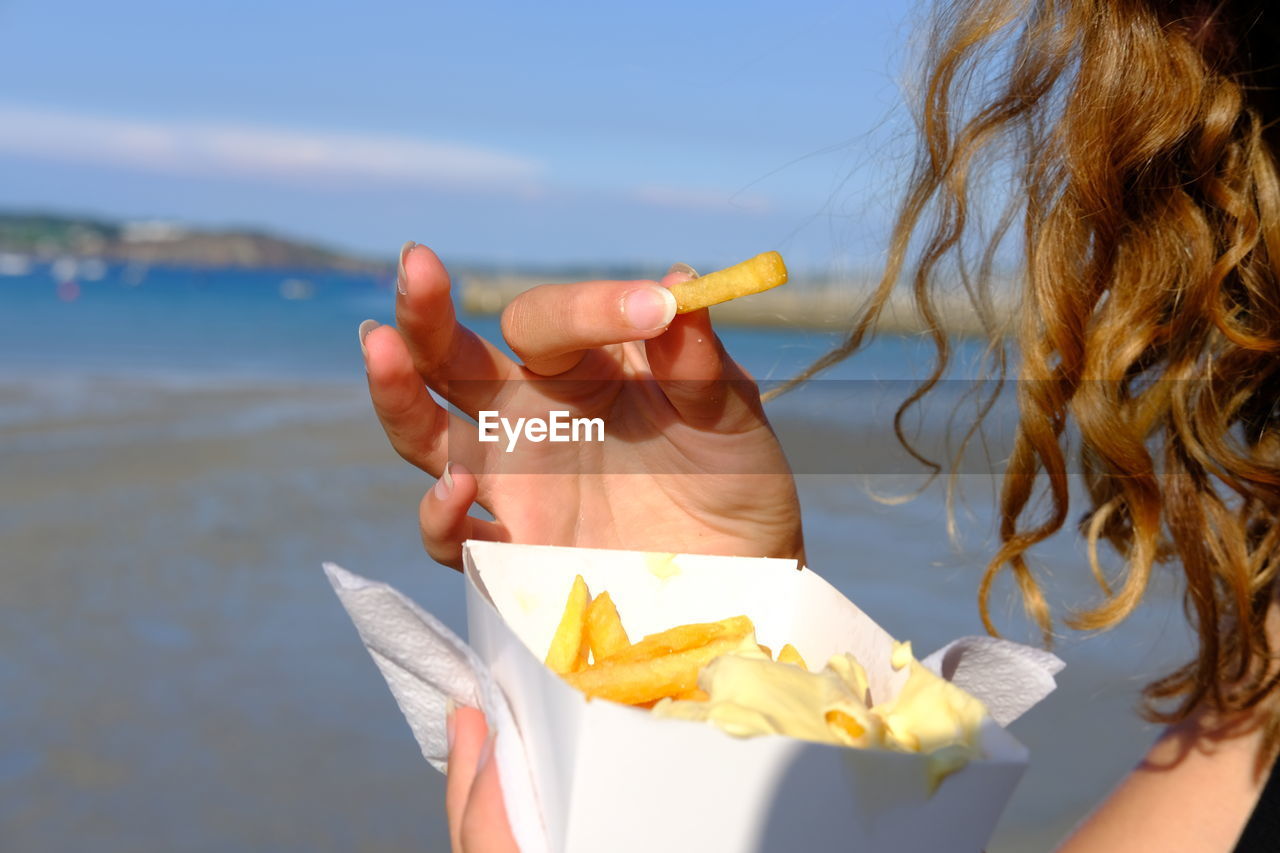 Close-up of woman holding food at beach against sky