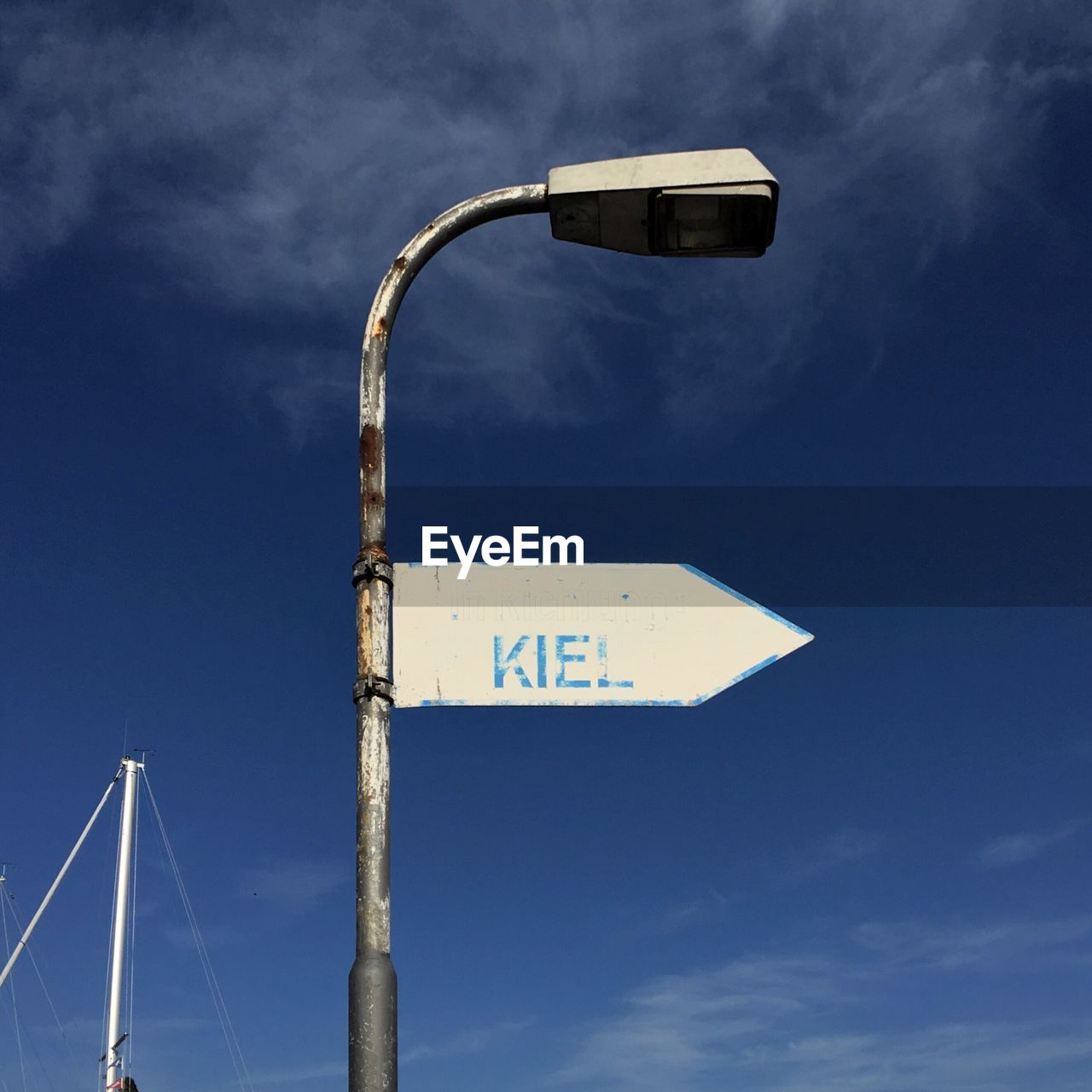 Low angle view of arrow symbol with text on street light against blue sky
