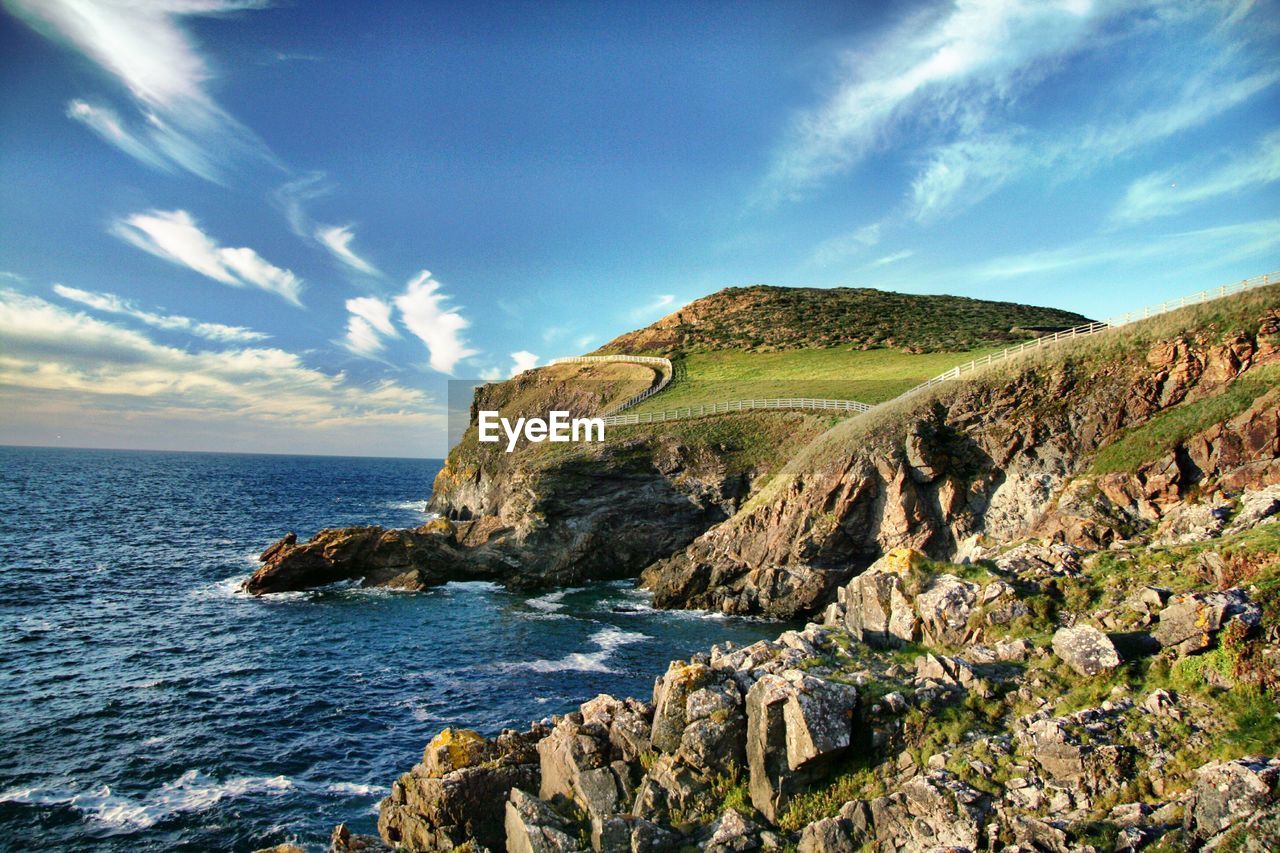 Scenic view of rocky, fenced, green coastline and sea in cornwall, uk