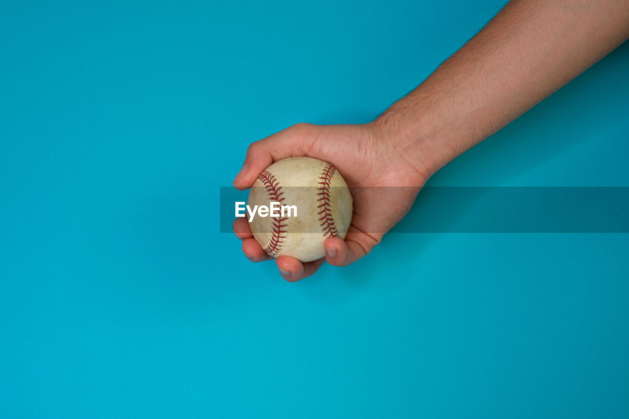 Close-up of hand holding a ball against blue background
