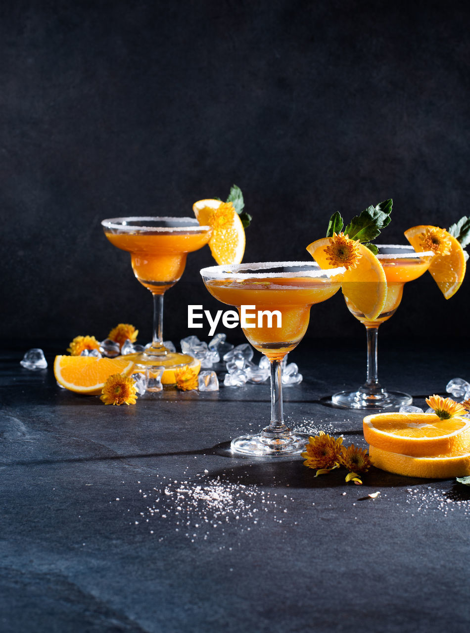 Glasses of orange cocktail decorated with orange and sugar on the edge of glass on black background