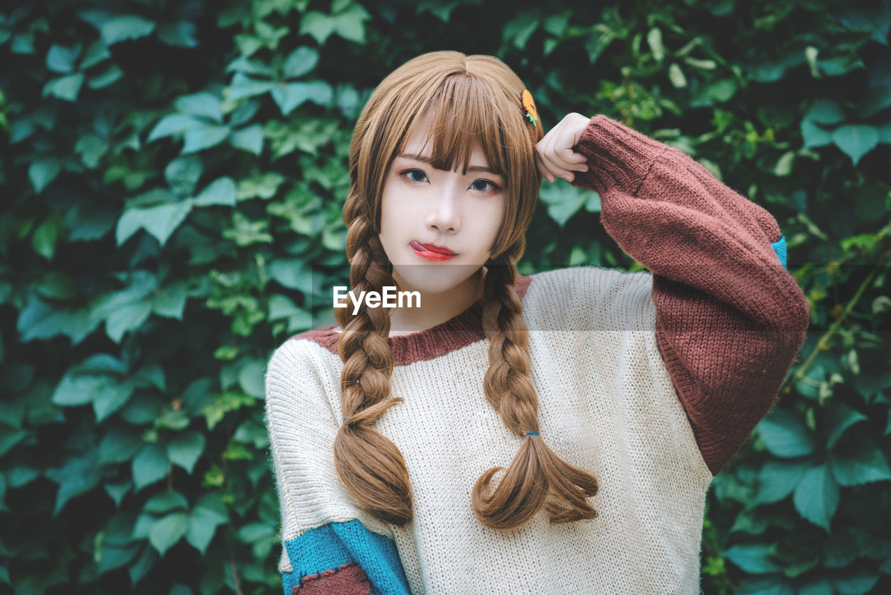 Portrait of young woman with braided hair standing against plants at park