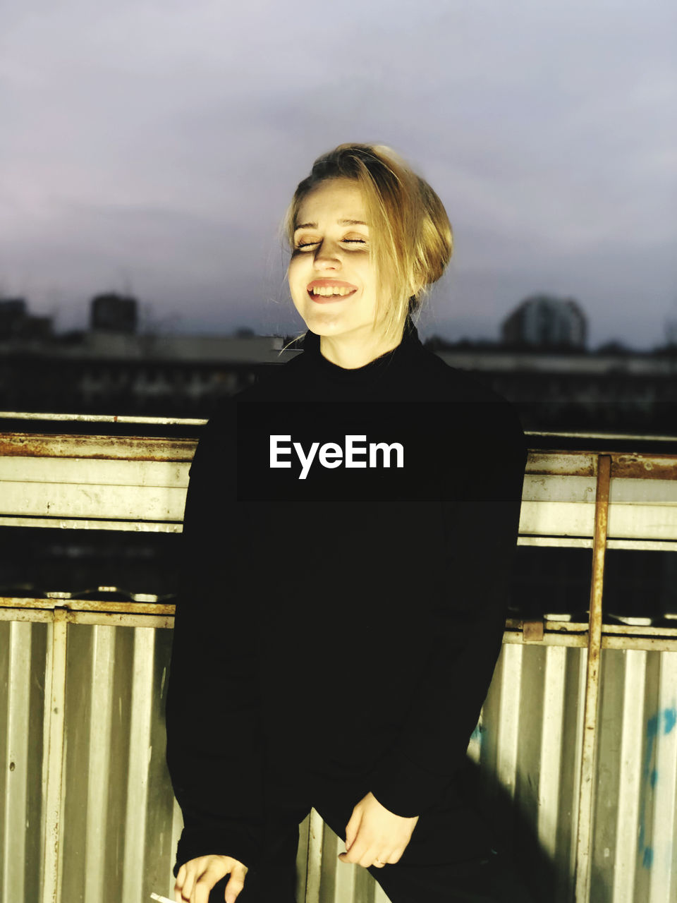 Smiling woman with eyes closed standing against railing