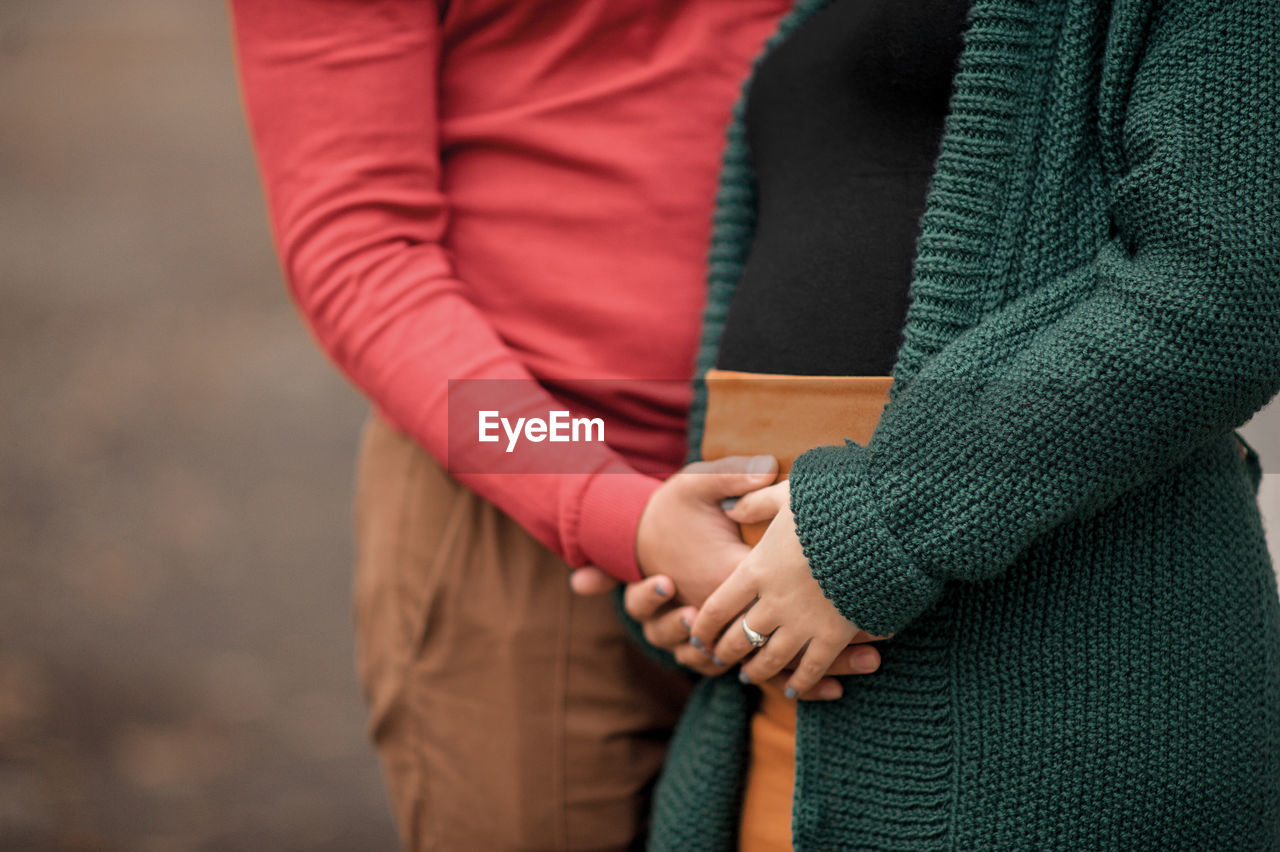 Man and woman hands hold pregnant woman tummy in atmosphere of autumn forest