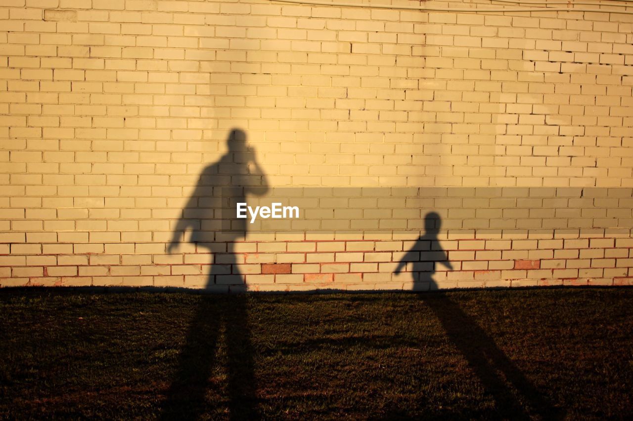 Shadow of man and boy on brick wall during sunny day