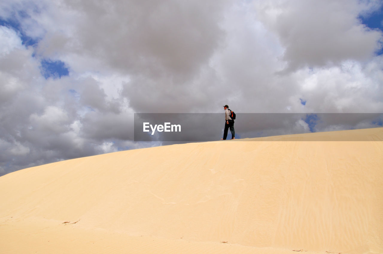 Low angle view of man walking at desert against cloudy sky