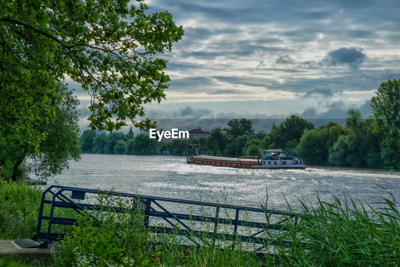 Boat sailing on river by trees against sky