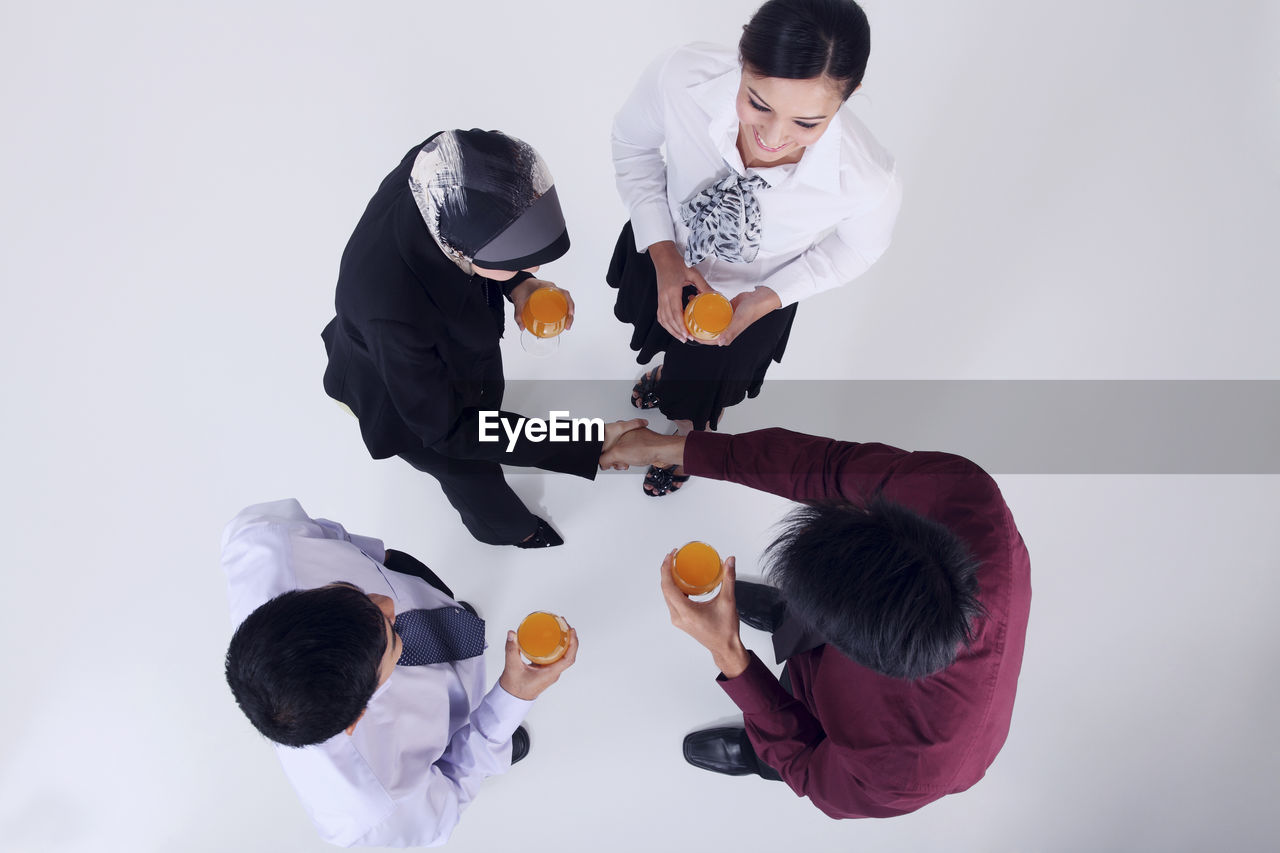 High angle view of business people holding drinks while standing over white background