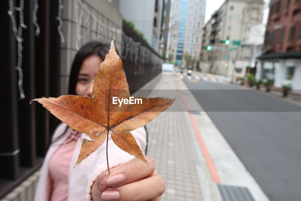 Close-up of woman holding leaf on sidewalk