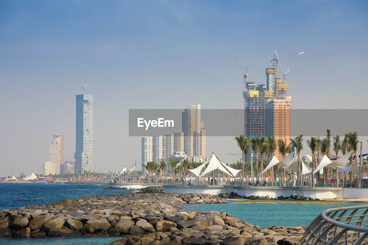 SEA BY MODERN BUILDINGS AGAINST SKY IN CITY