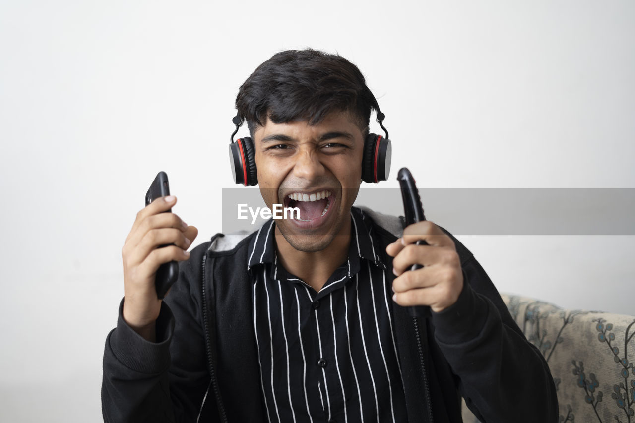 Indian cute teenager wearing black jacket, wireless headphone,holding cell phone,remote