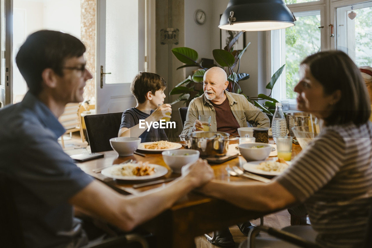 Grandfather and grandson having juice while sitting with family at dining table in home