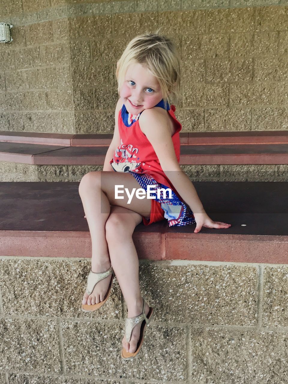 Portrait of cute girl sitting on retaining wall