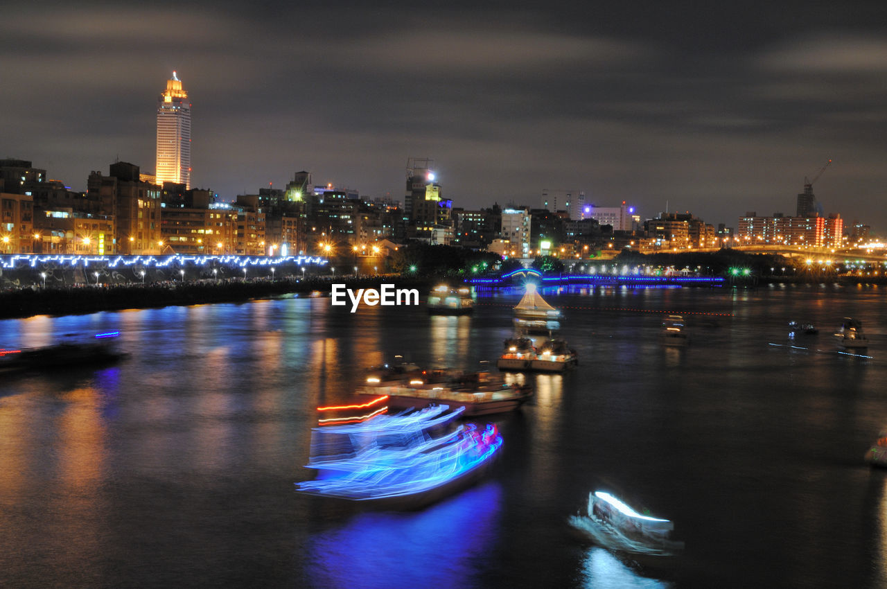 ILLUMINATED BUILDINGS BY RIVER AT NIGHT