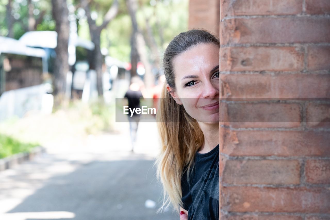 Portrait of smiling young woman standing behind brick wall