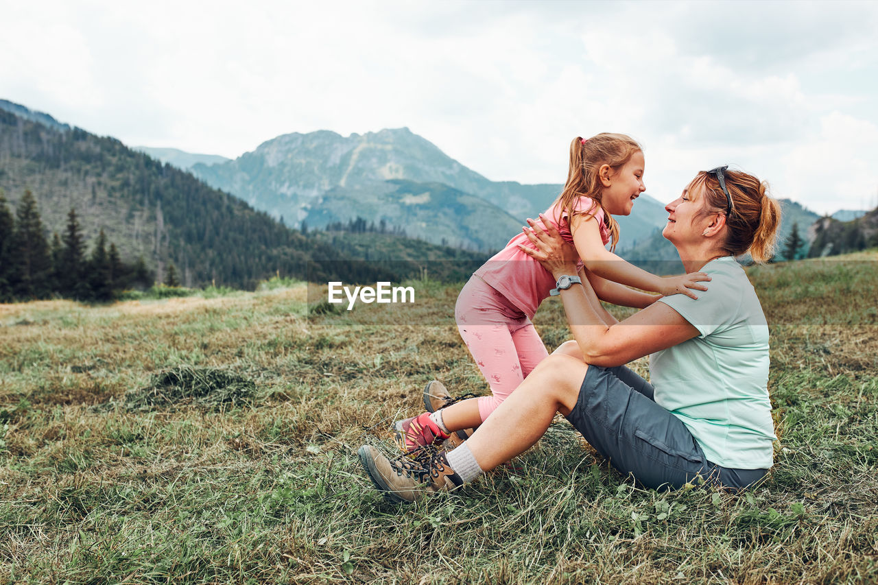 Little girl playing with her mother on grass enjoying summer day. happy family playing in the field