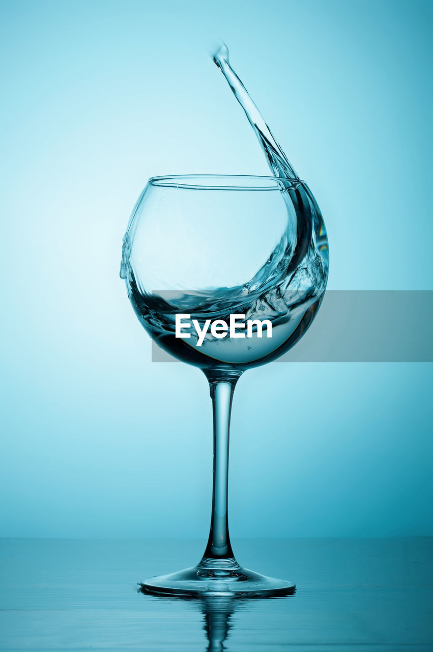 Close-up of water and ice cubes in glass over blue background