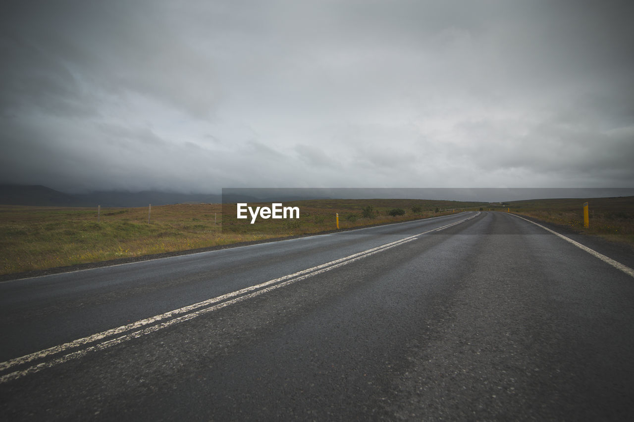 Empty road amidst field against cloudy sky