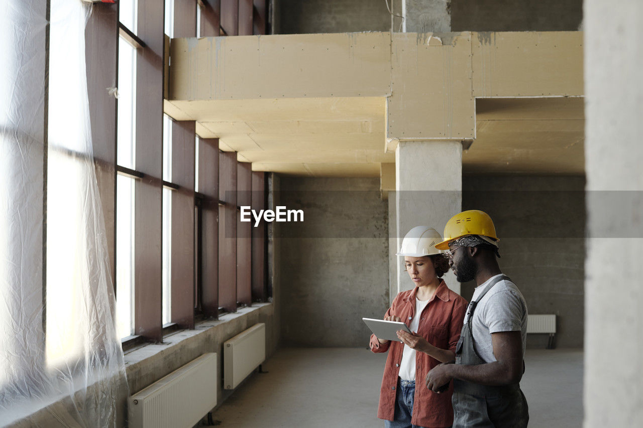 Engineer using tablet pc and discussing with coworker at construction site