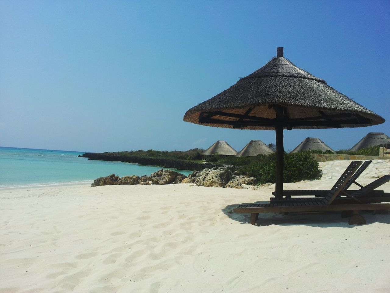 Lounge chair and sunshade on beach against clear sky