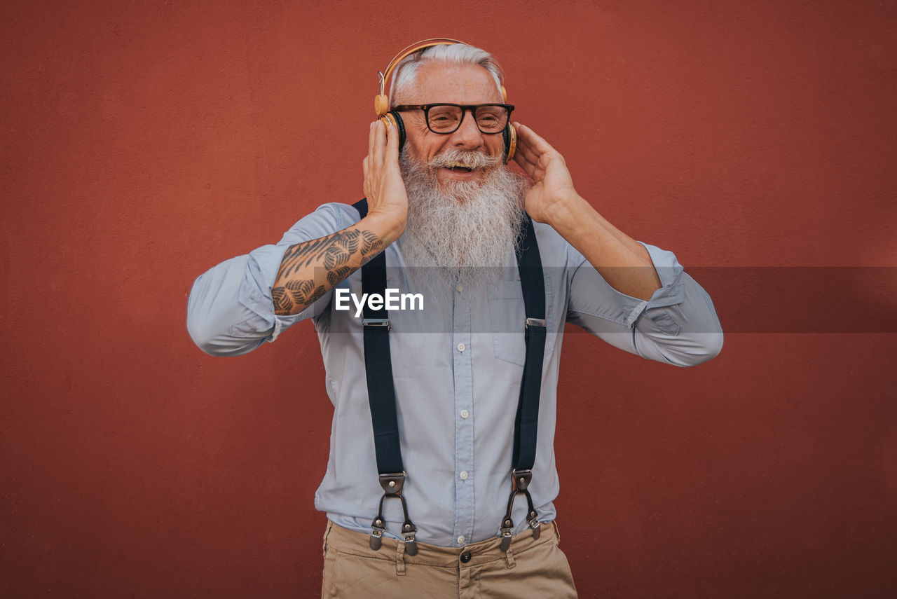 An older man in hipster clothes and glasses and long white beard listens to music