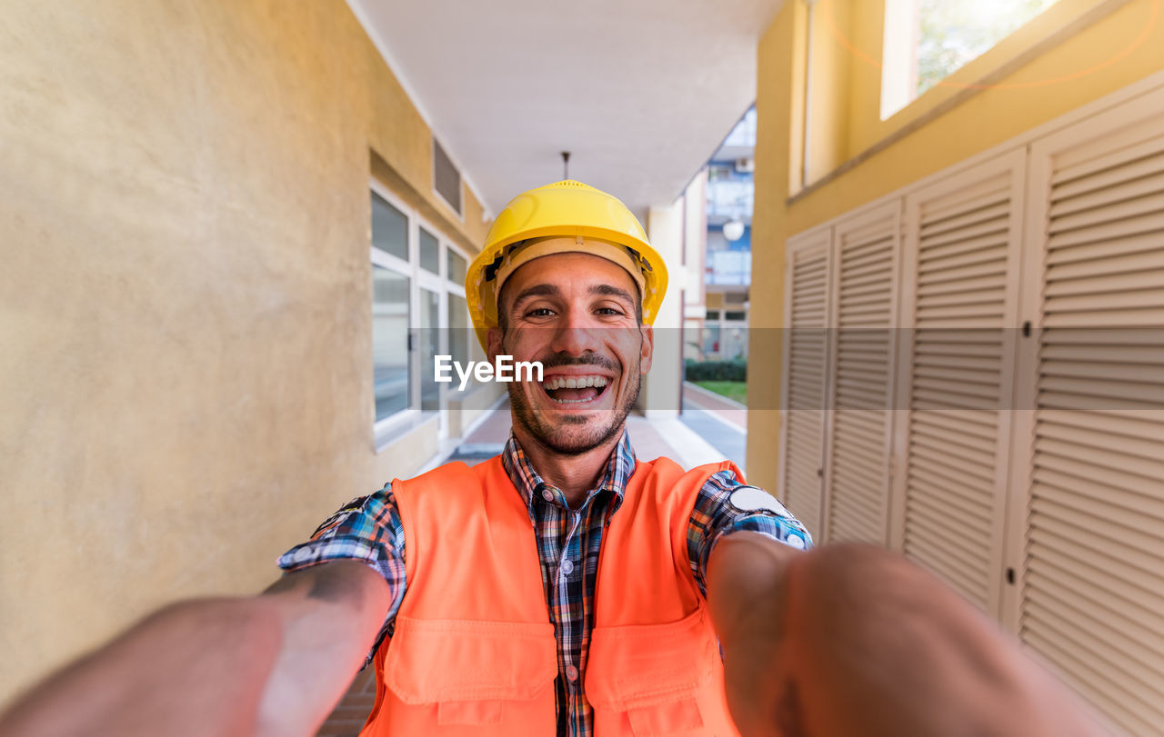 PORTRAIT OF SMILING MAN STANDING AGAINST WALL