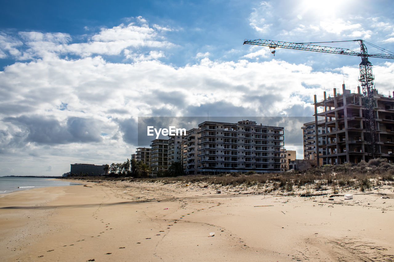 sky, land, beach, sea, architecture, water, sand, cloud, built structure, nature, coast, horizon, ocean, construction industry, building exterior, city, building, industry, body of water, shore, construction site, no people, outdoors, machinery, travel destinations, development, travel, day, blue, crane - construction machinery, landscape