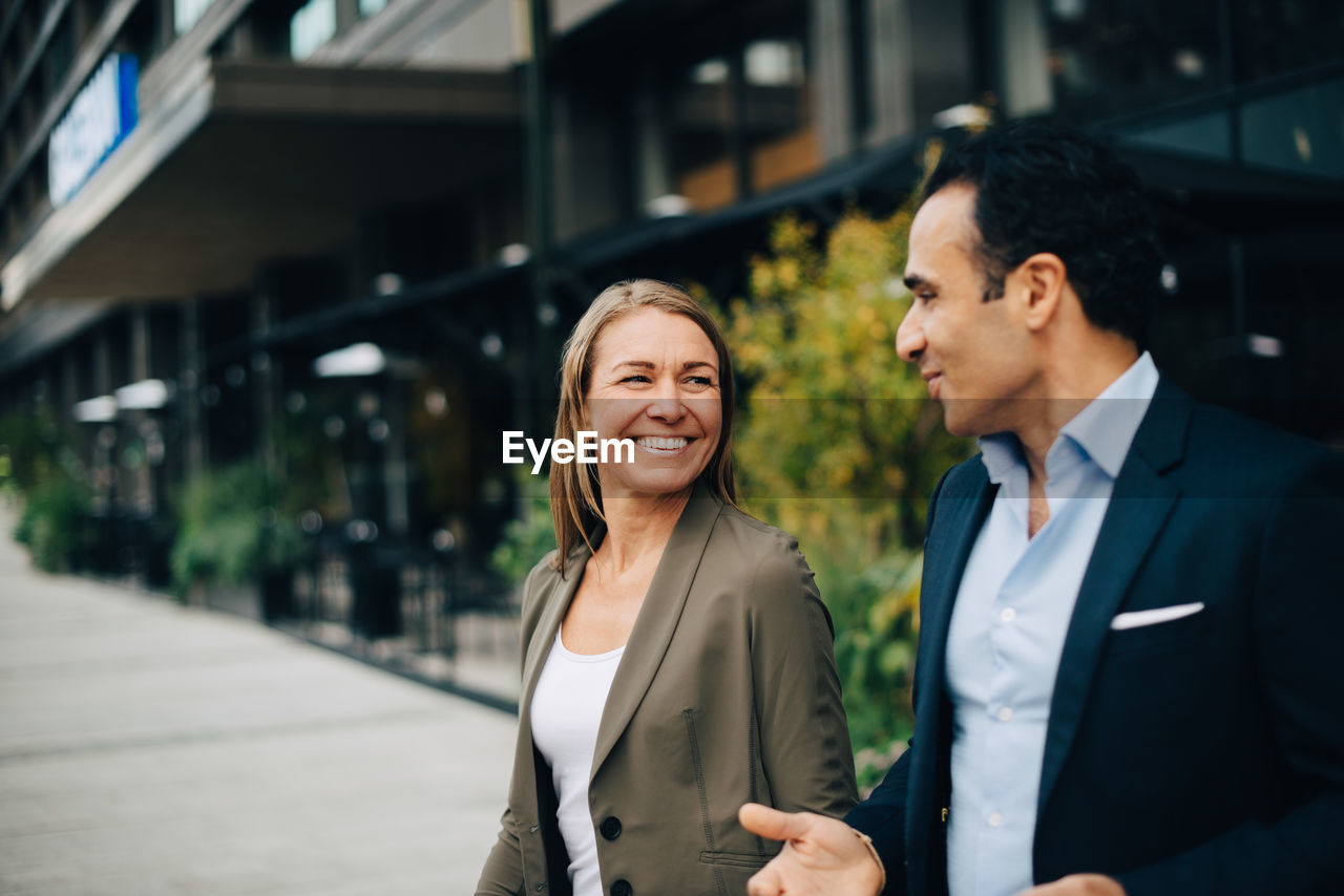 Smiling mature business colleagues talking while walking in city