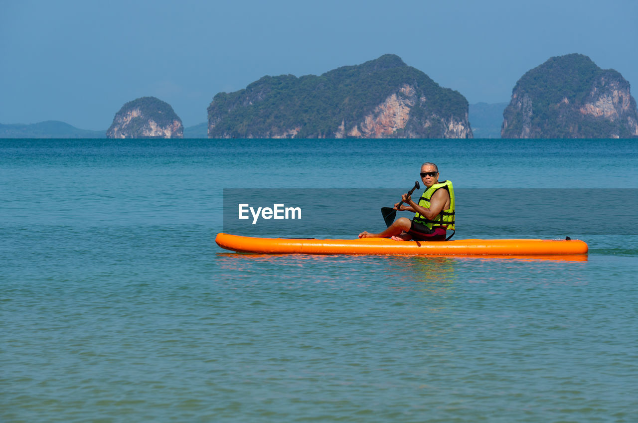 Senior asian man playing paddle board in blue sea during summer vacation