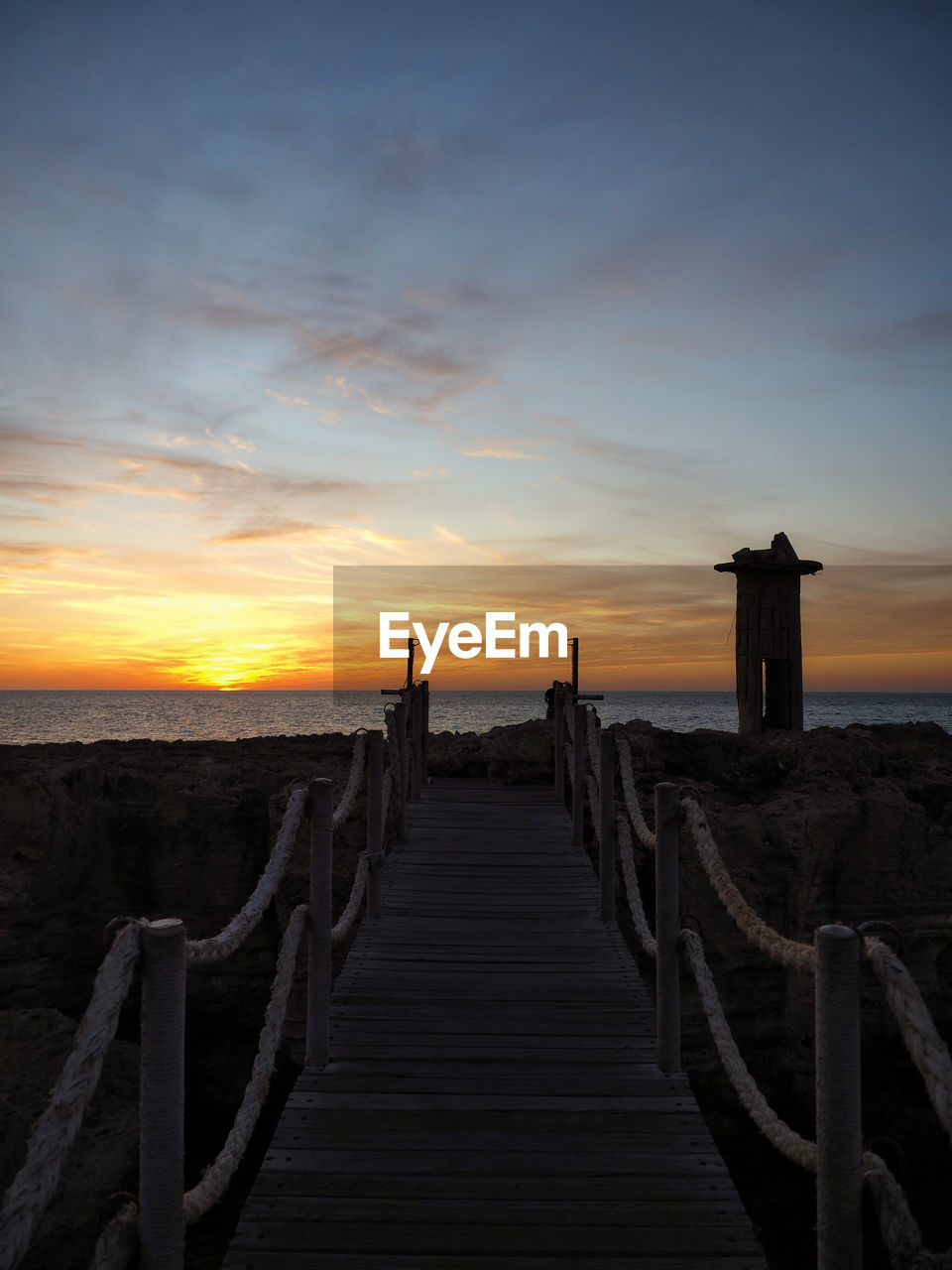 WOODEN POSTS AT SEA AGAINST SKY DURING SUNSET