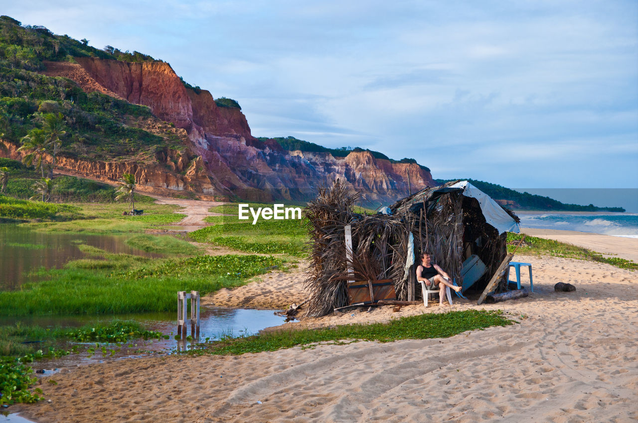 Man sitting on chair by tent at beach against sky