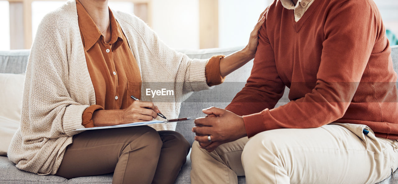 midsection of doctor explaining to customer on sofa at home