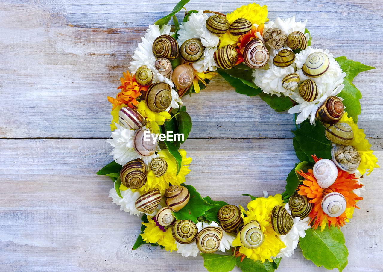 High angle view of homemade flower wreath with empty snail shell on table for decoration