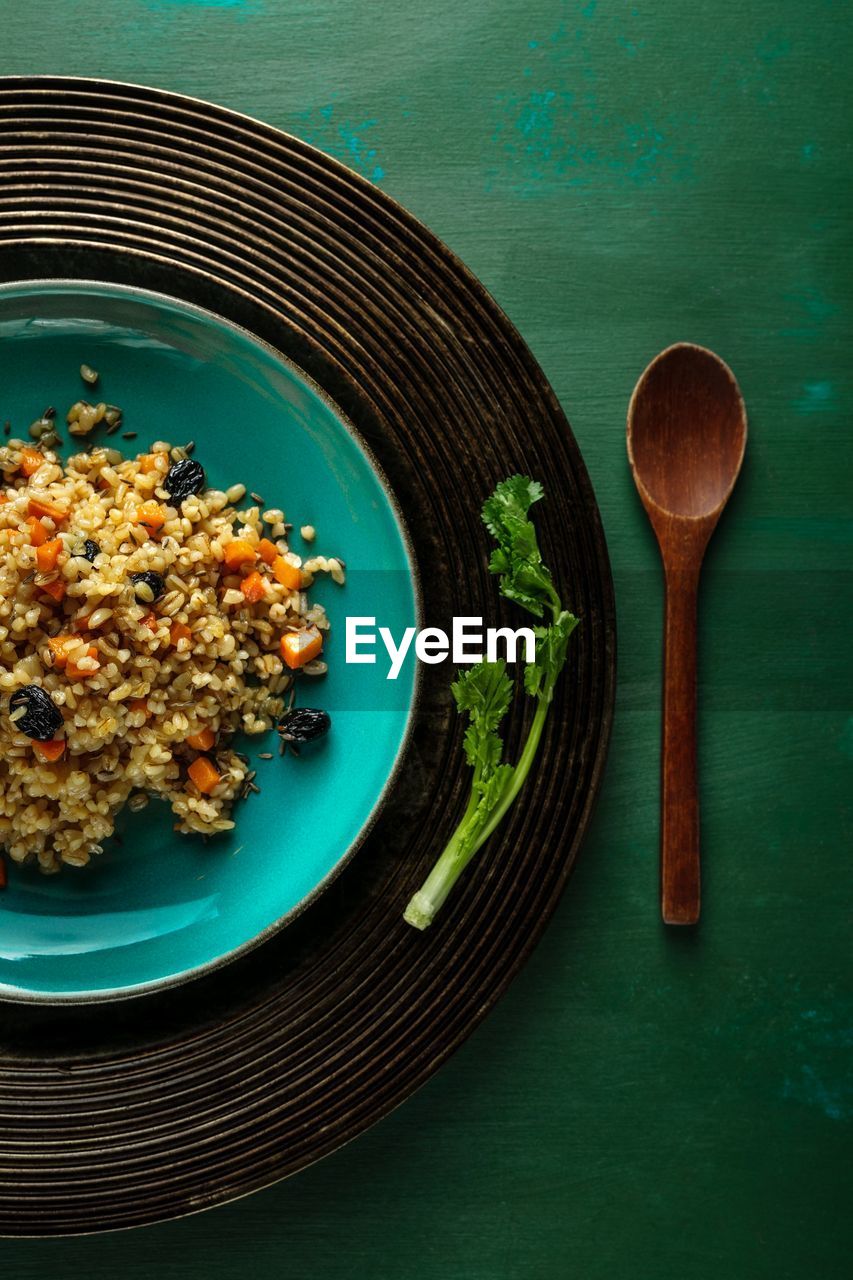 Vegan pilaf in teal colored plate on green background. top view, closeup