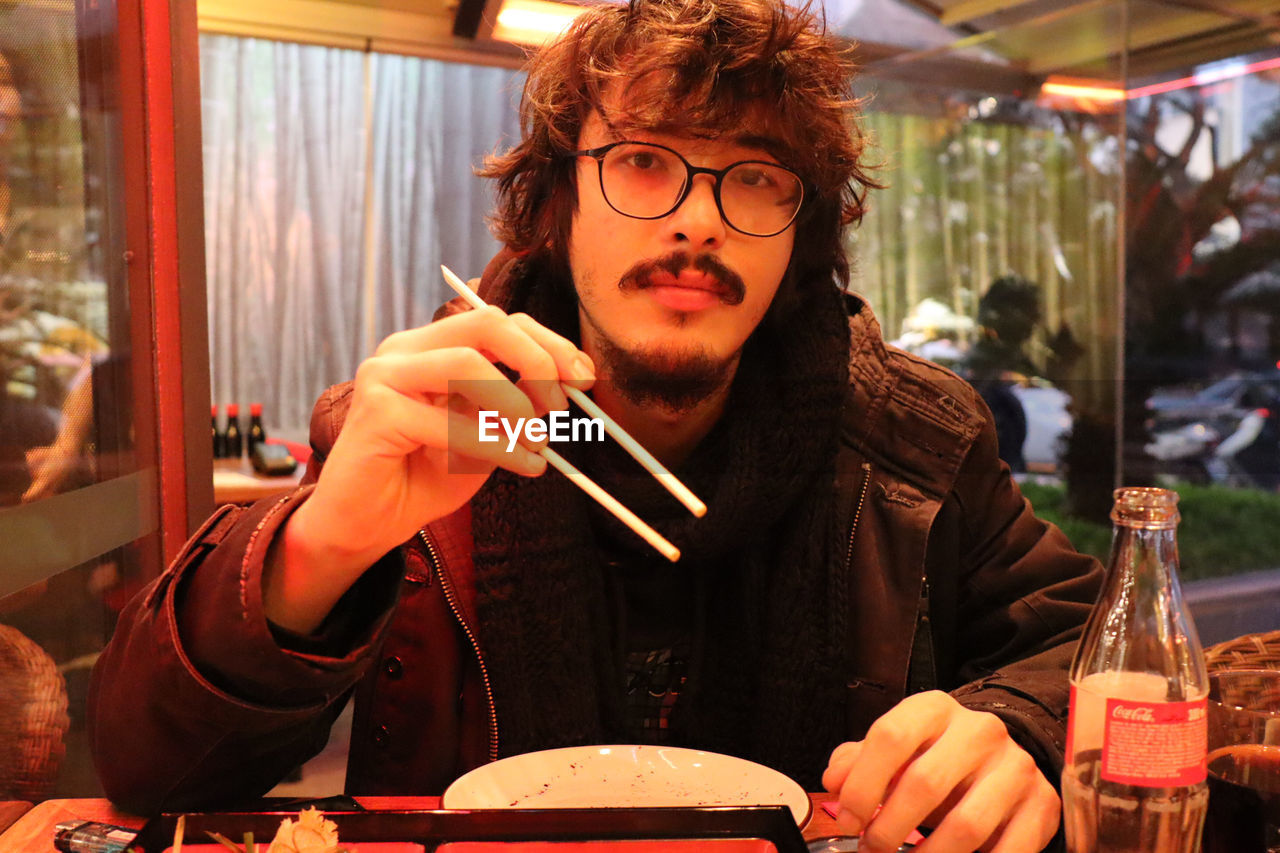 Portrait of man holding chopsticks at restaurant